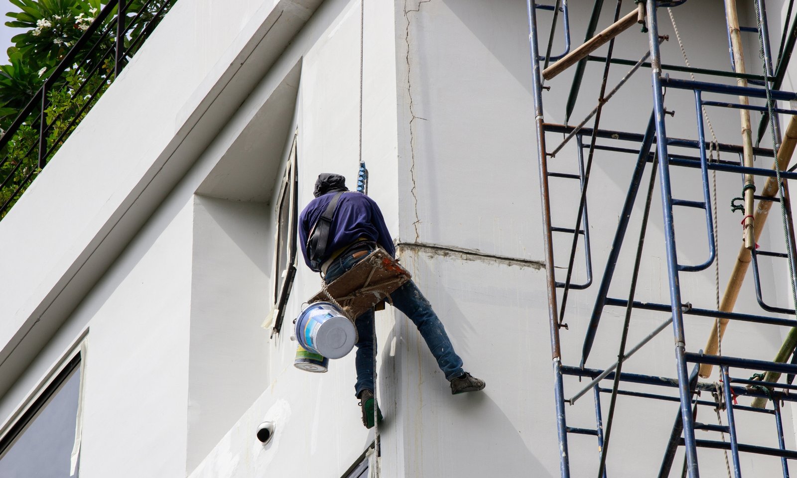 Bouwvakker die gevelschilderwerk uitvoert op een hoog gebouw