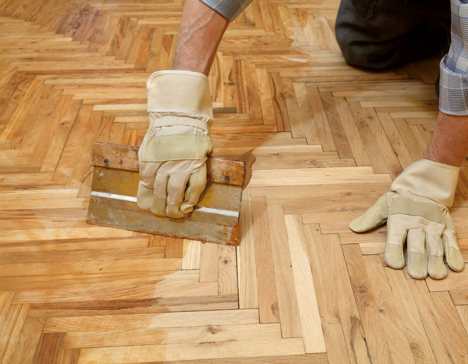 Een vakman brengt vernis aan op een houten parketvloer