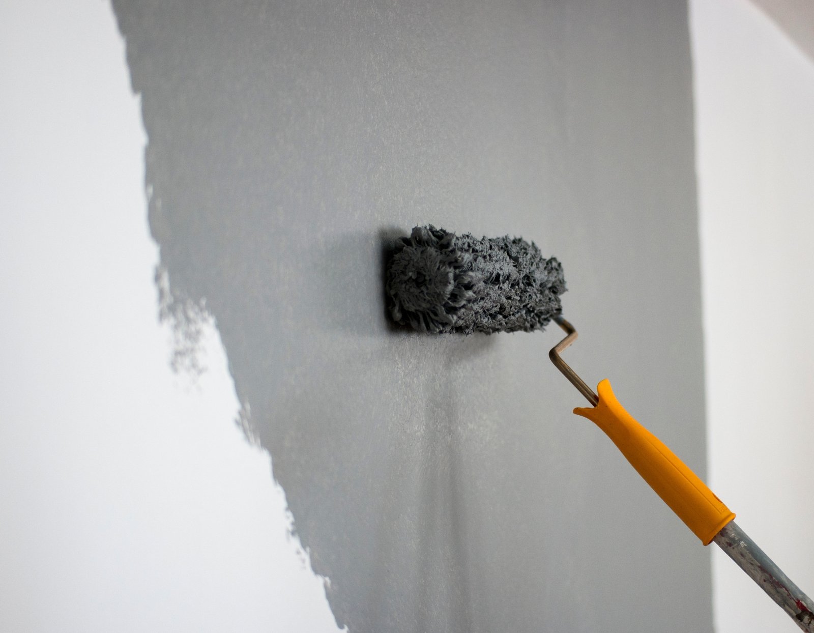 Een verfroller die grijze verf verspreidt op een muur, met een gelijkmatige dekking op een binnenoppervlak.