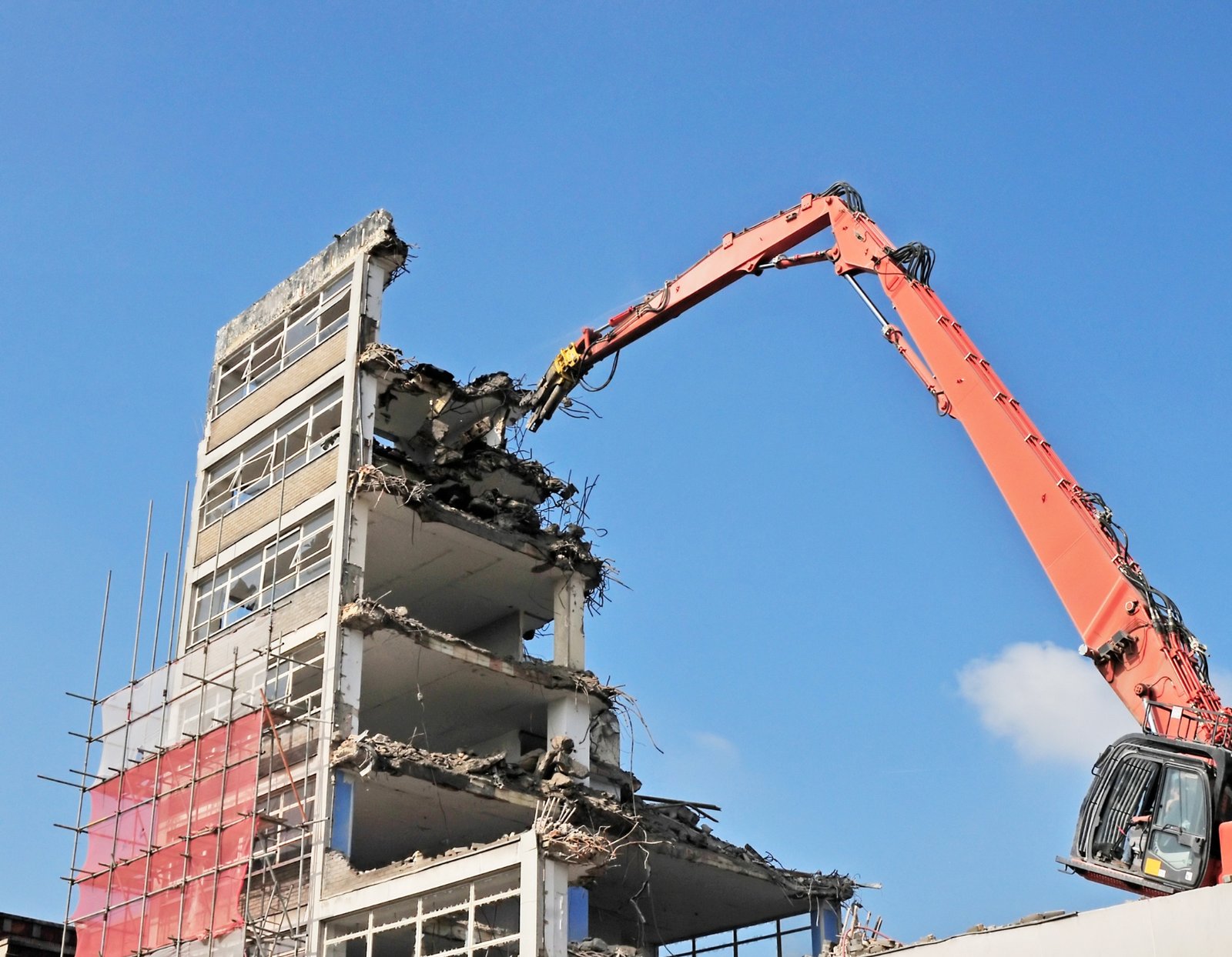 Graafmachine die een gebouw sloopt onder een heldere hemel.